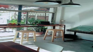 Un espace de travail comprenant une table, deux tabourets, une table à dessin et une grande fenêtre donnant sur un paysage verdoyant.