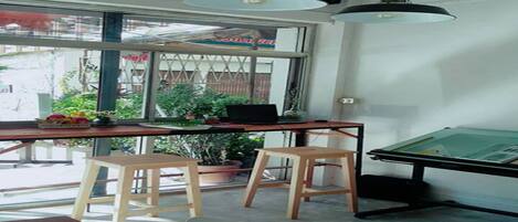 A workspace with a table, two stools, a drafting table, and a large window with a view of greenery outside.