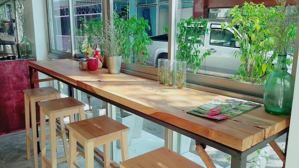Un coin bar en bois, avec des tabourets et une fenêtre donnant sur les voitures garées et la verdure à l’extérieur.