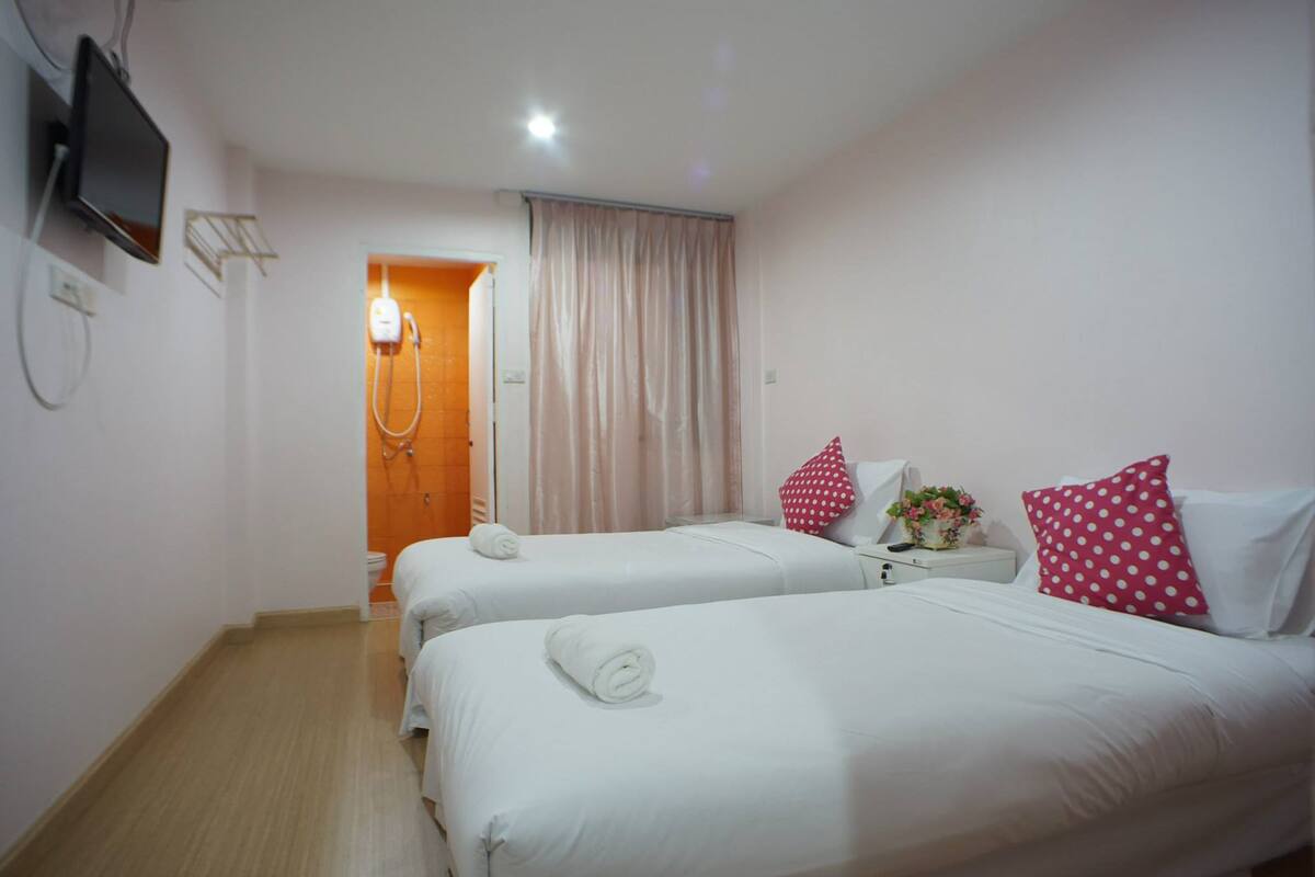 Quarto de hotel com duas camas, uma televisão fixada na parede e um banheiro visível por uma porta aberta.