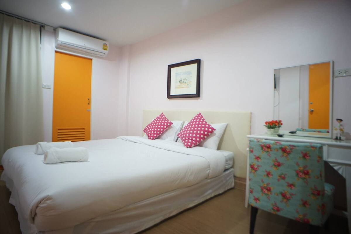 Quarto de hotel com cama, almofadas, escrivaninha, espelho e ar condicionado.