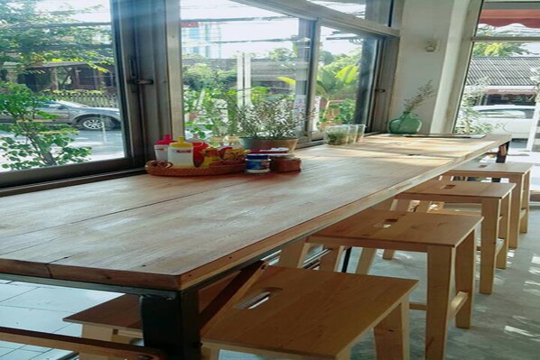 Une table en bois avec des bancs, dans une pièce dotée de grandes fenêtres.