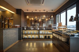A modern bar area with a variety of bottles and glasses, a buffet with plates and bowls, and hanging pendant lights.