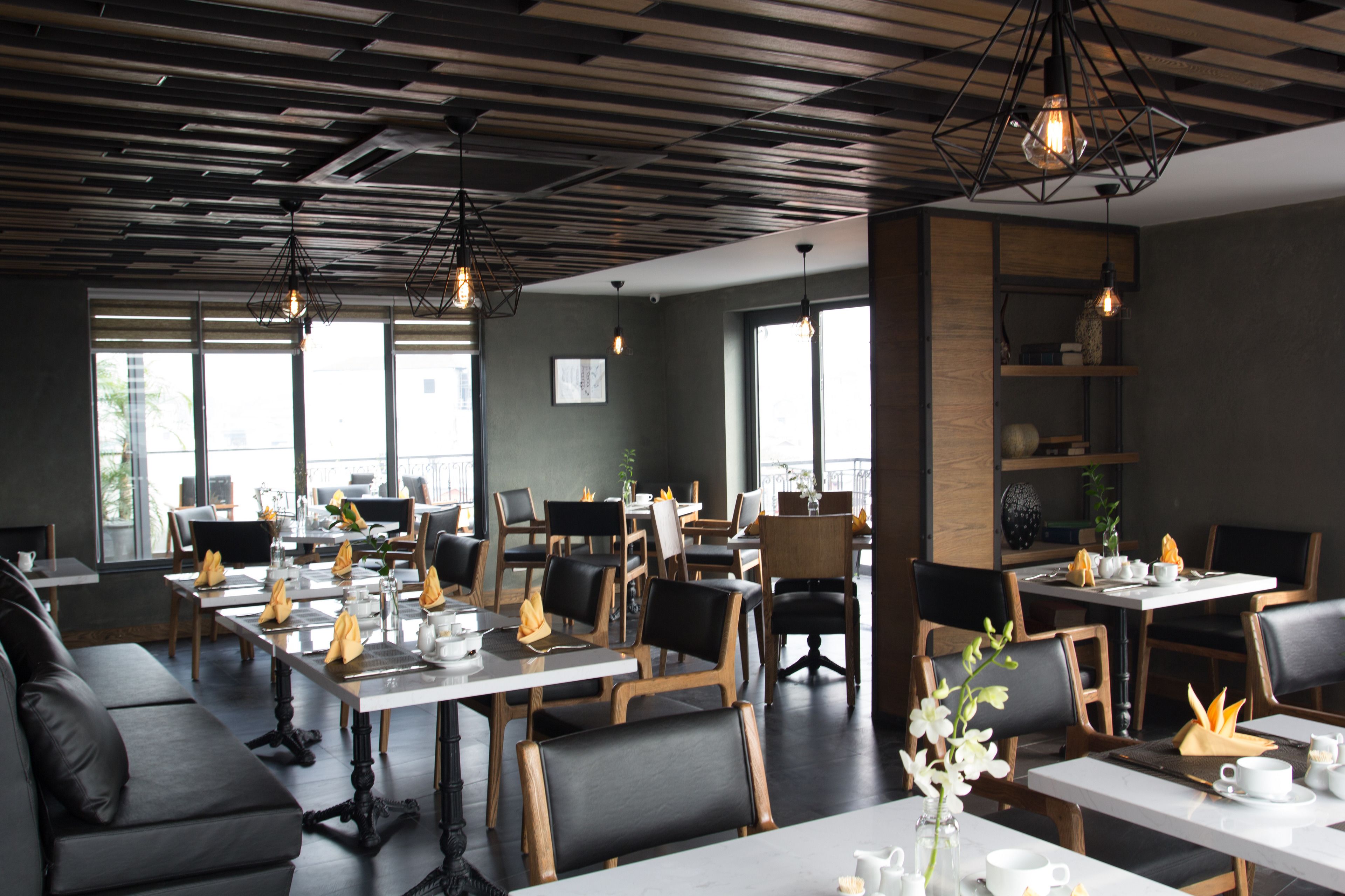 En modern restaurang med träpanel i taket, bord täckta med vita dukar, svarta stolar och hängande taklampor.
