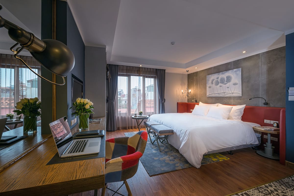 A hotel room with a bed, desk, chair, laptop, and a view of the city.