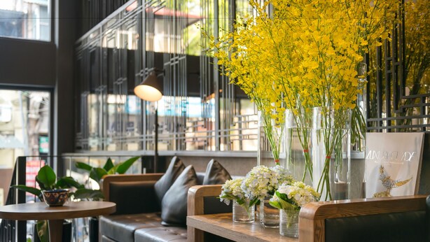 A modern interior with a wooden bench, a cushioned seating area, and a table with vases of flowers. - Bespoke Trendy Hotel Hanoi (Hanoi)