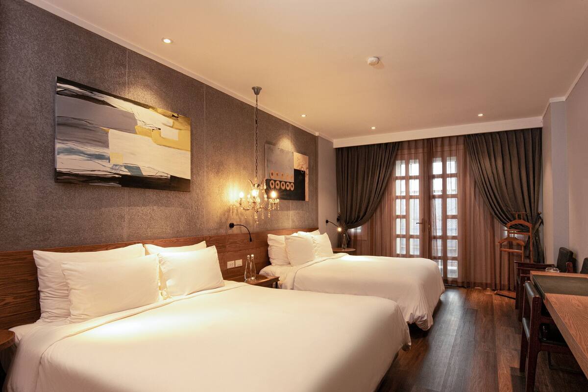 A hotel room with two beds, a large abstract painting, a chandelier, and a view of the outside through large windows.