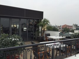 A rooftop terrace with a dining area, potted plants, and a view of the cityscape.