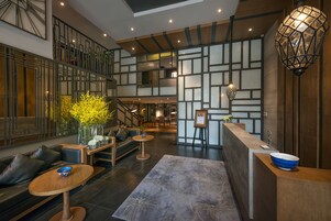 A modern hotel lobby with a seating area, a reception desk, and a staircase.