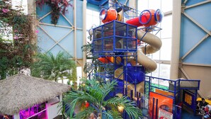 An indoor play area with a climbing structure, a thatched-roof hut, and indoor plants. - L'Hôtel Québec par JARO (Québec City)