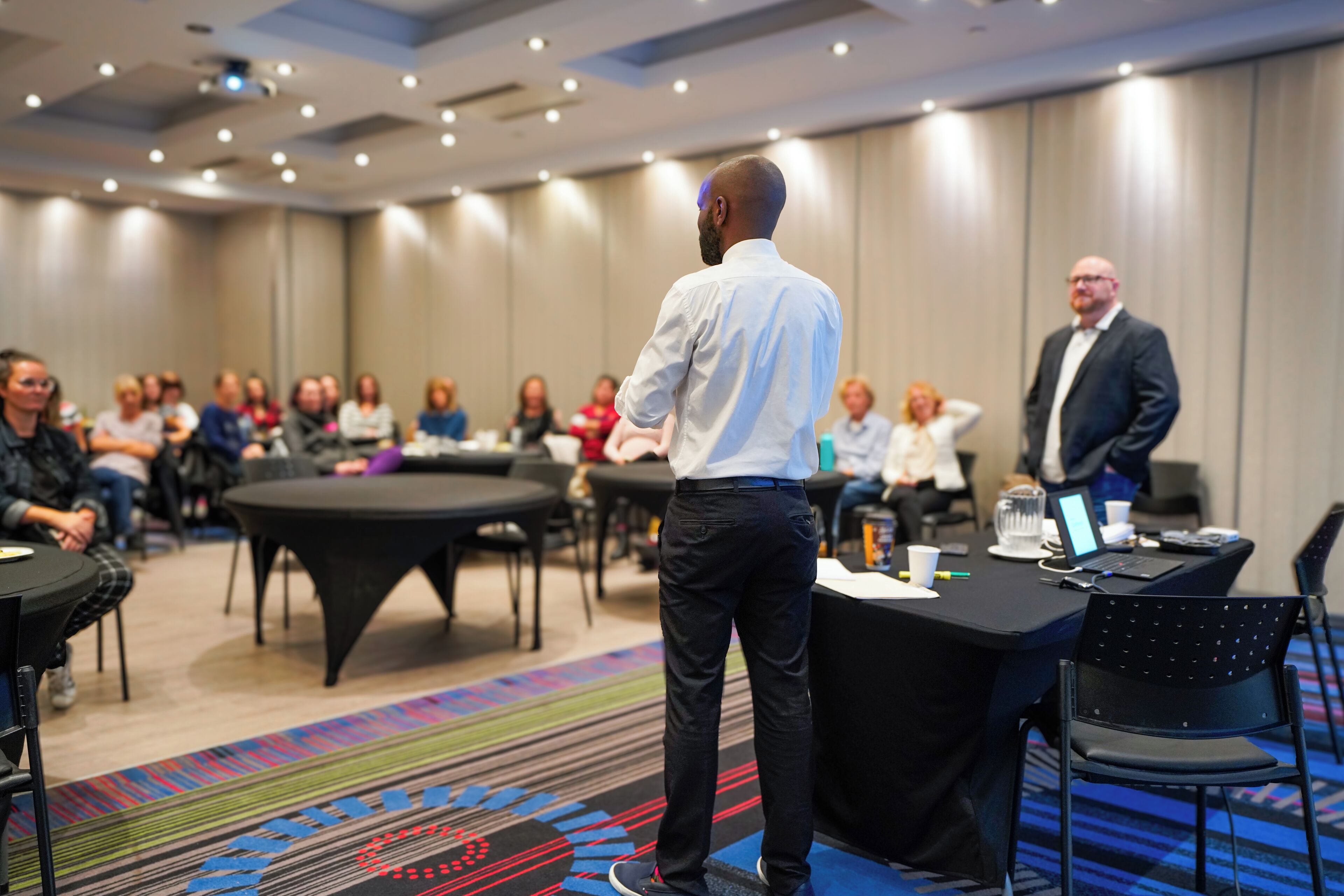A conference room with a round table, chairs, and attendees seated around.