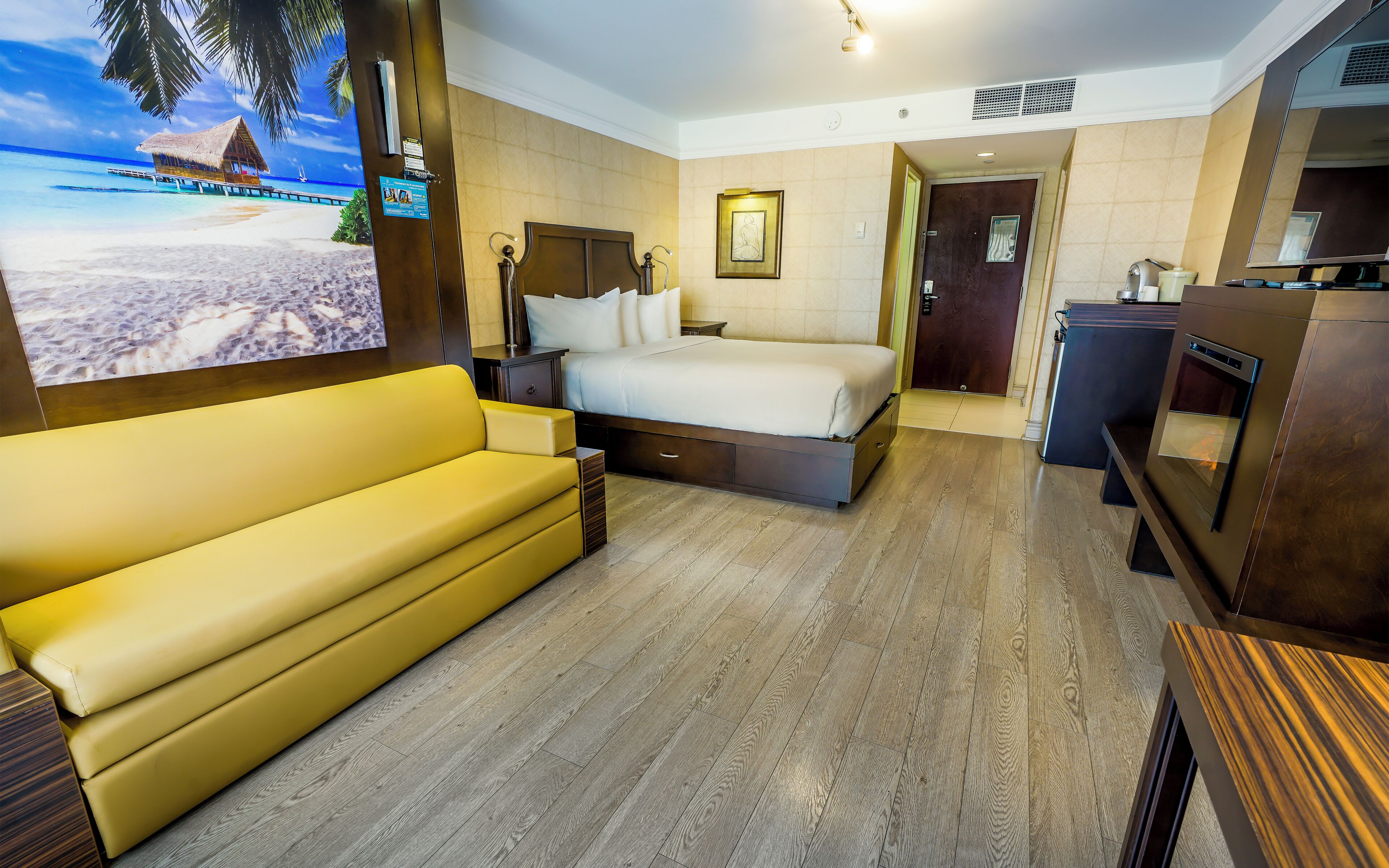 Habitación de hotel con cama, sofá, televisión y suelo de madera.