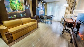 Habitación de hotel con sofá, escritorio y silla, y un televisor de pared grande mostrando un loro.