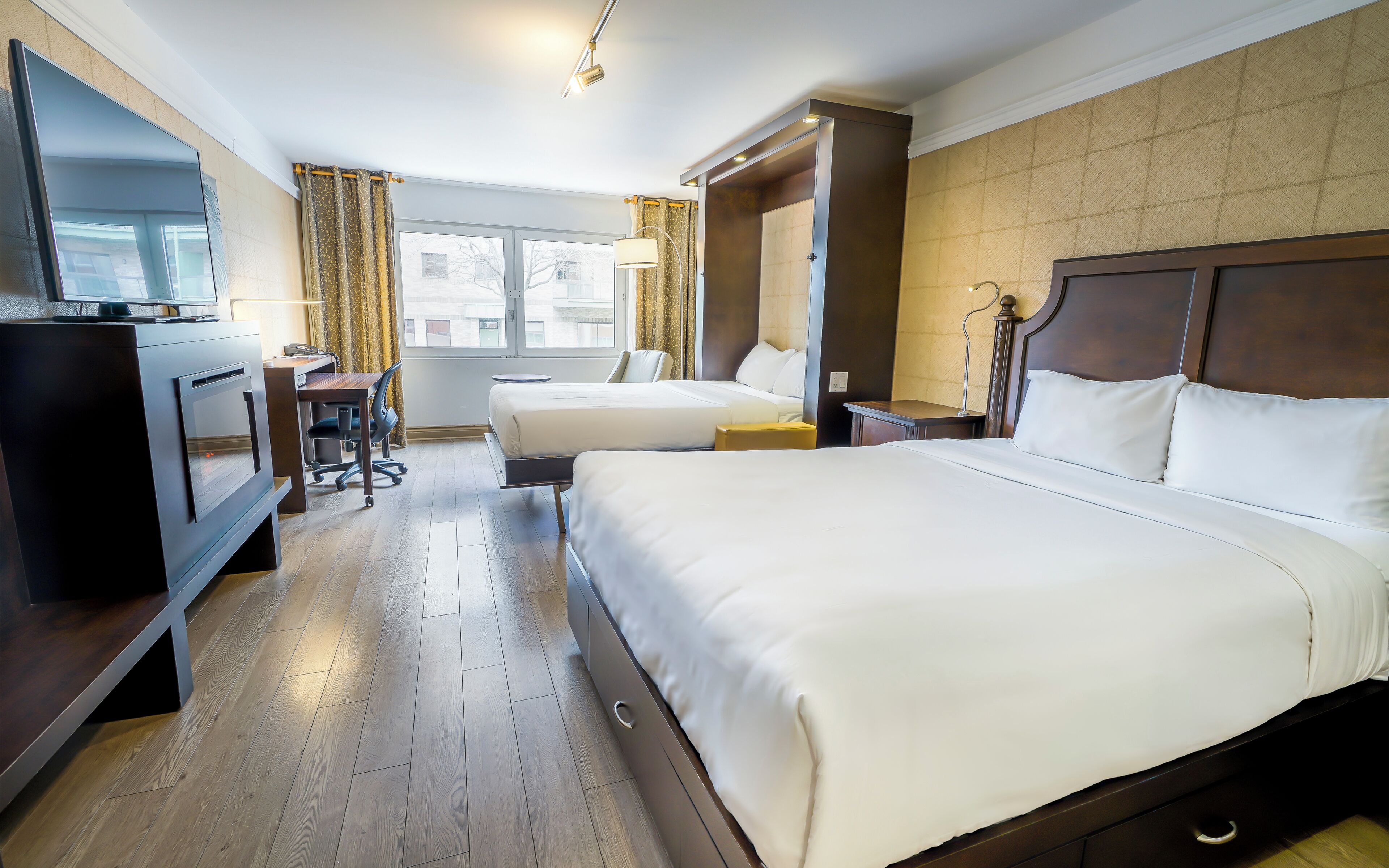 Une chambre d’hôtel avec deux lits, un bureau, une chaise, une télévision et une fenêtre avec des rideaux.