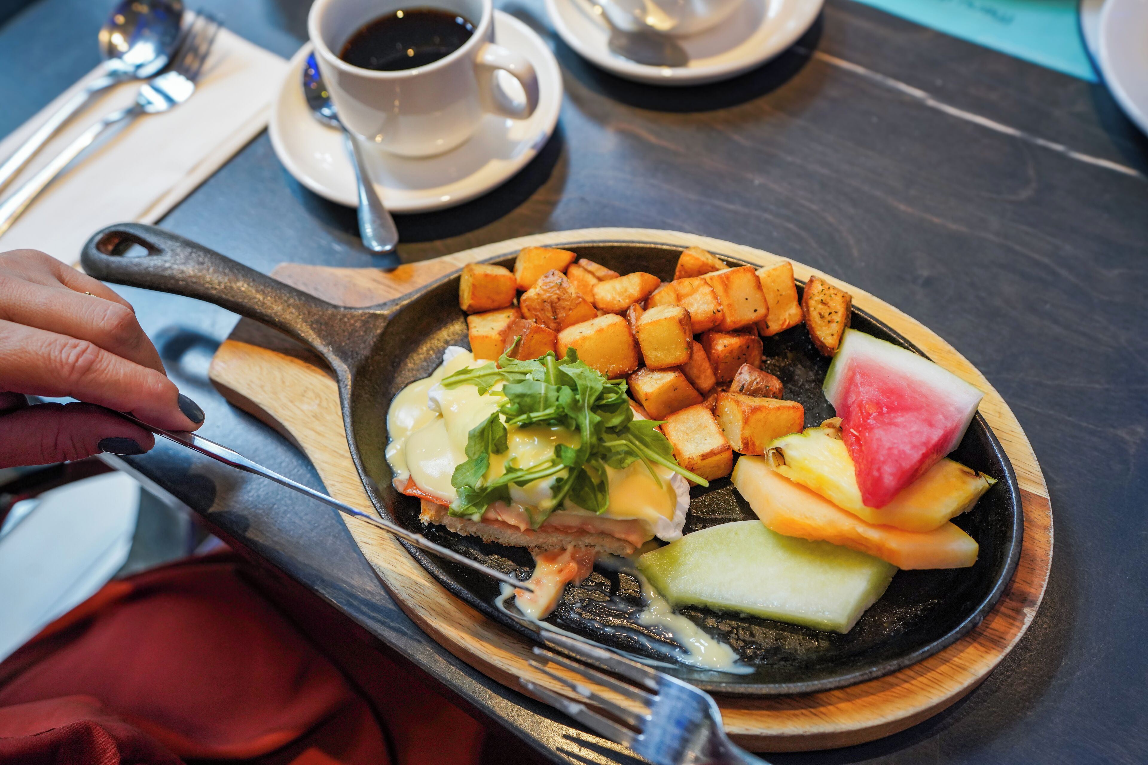 A breakfast plate with eggs, greens, and fruit on a wooden board.