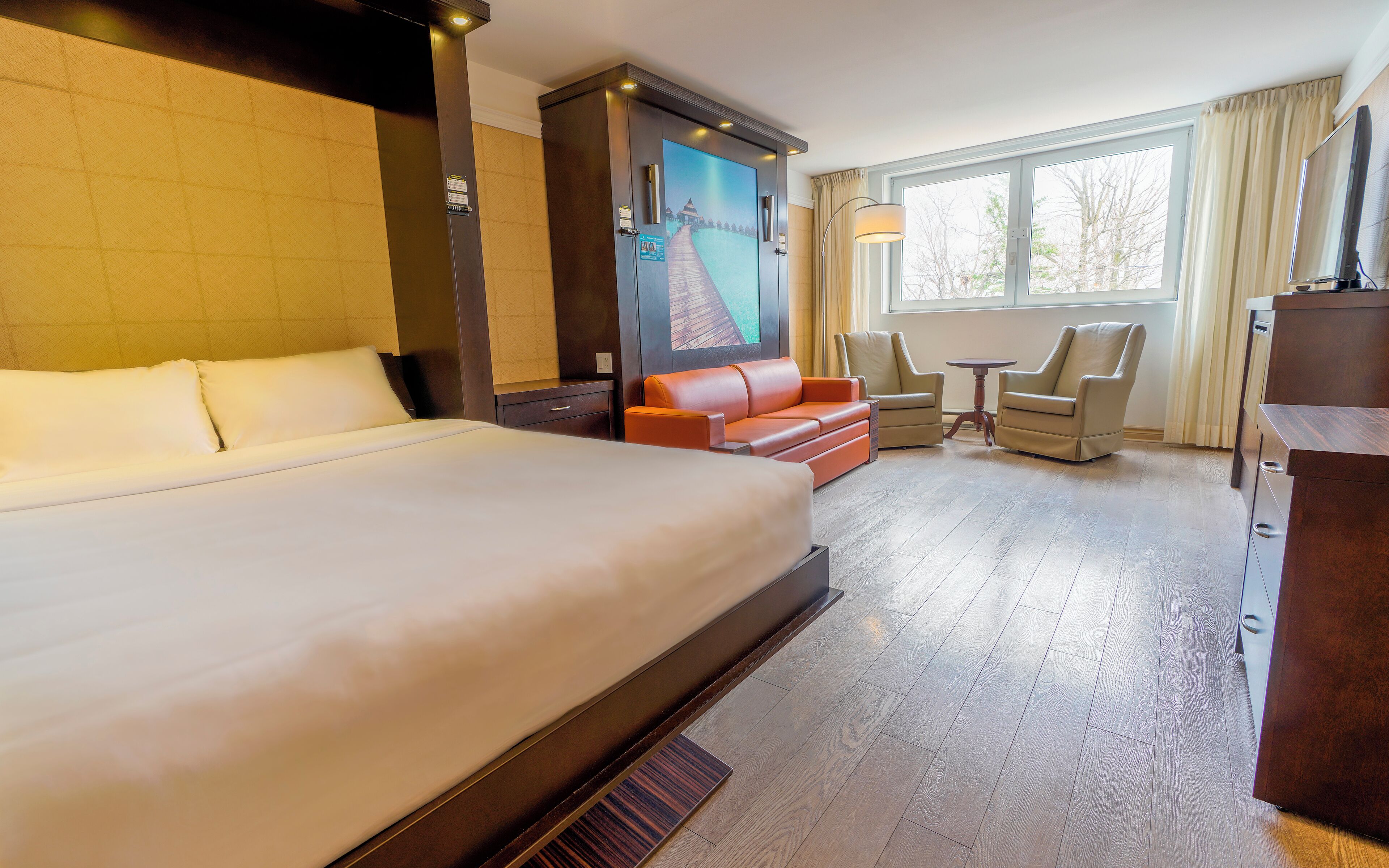 Une chambre d’hôtel avec un grand lit, un canapé, deux fauteuils, une petite table et un téléviseur.