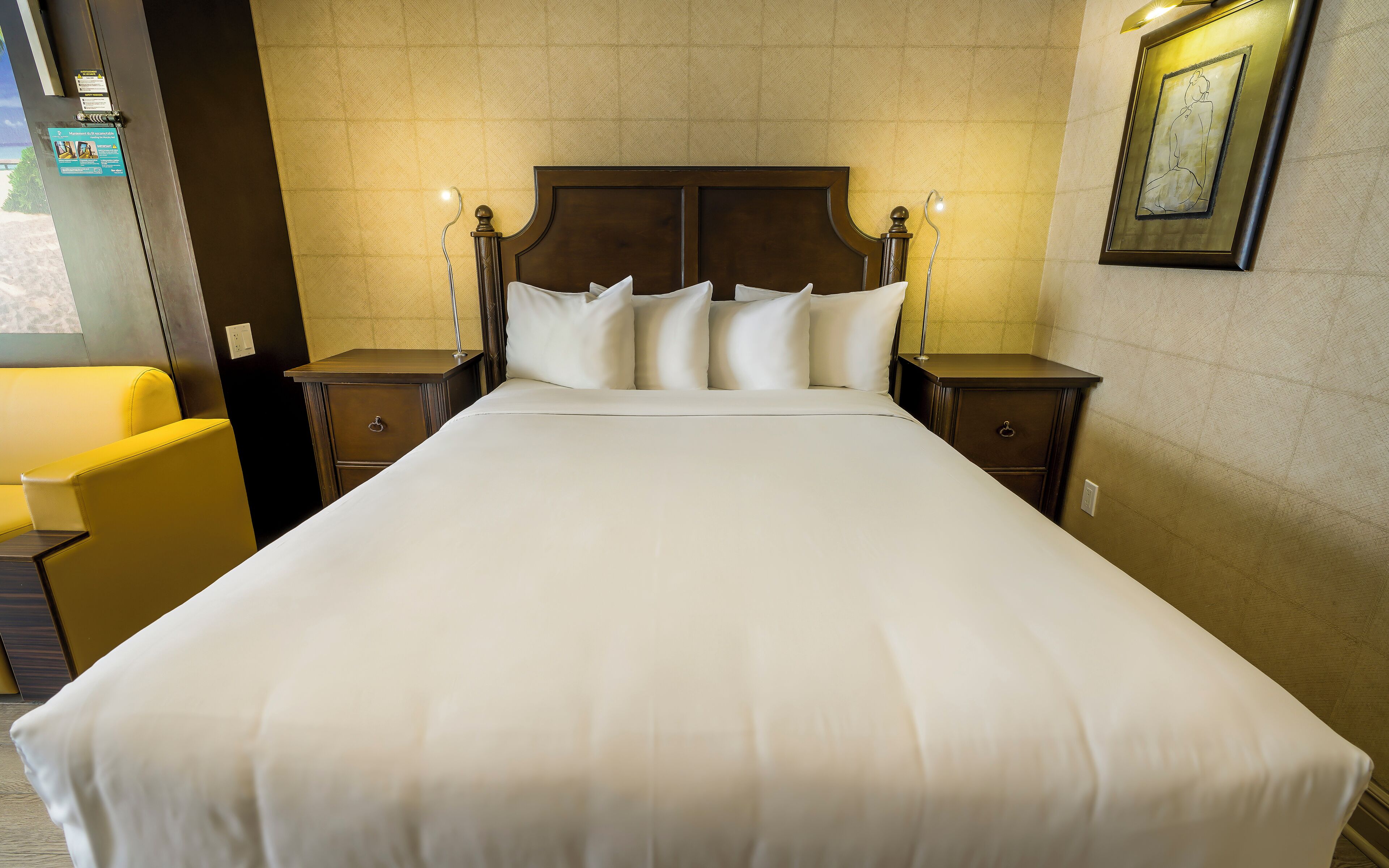 Une chambre d’hôtel avec un grand lit, deux tables de chevet, une petite table, une chaise et un tableau encadré au mur.