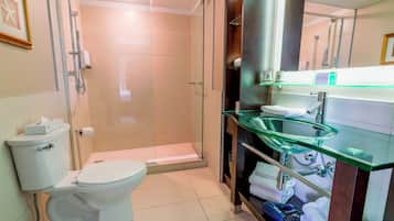 Un baño moderno con cabina de ducha de vidrio, inodoro y lavamanos de vidrio, además de un perchero.