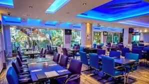 A restaurant with multiple tables and chairs, large windows with a view of greenery, and a staircase leading to an upper level. - L'Hôtel Québec par JARO (Québec City)