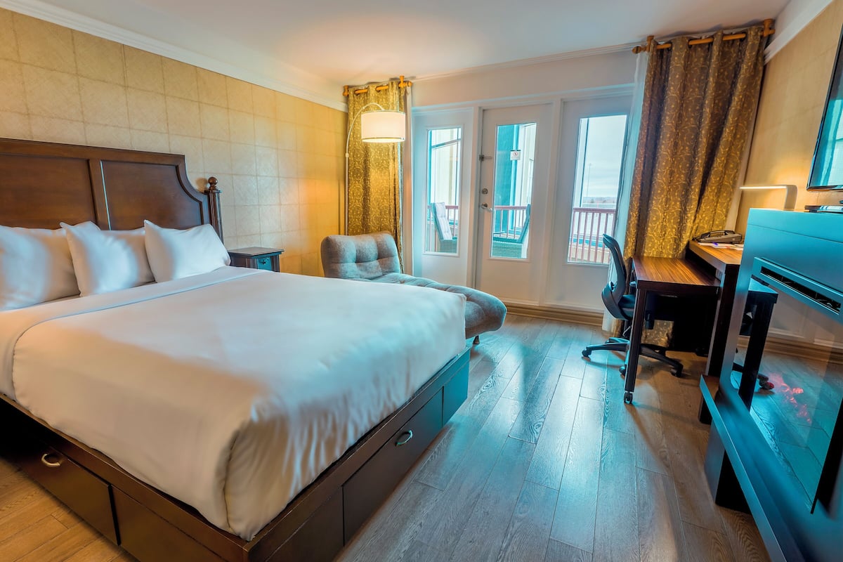 A hotel room with a large bed, a desk, a chair, and a balcony with a view.