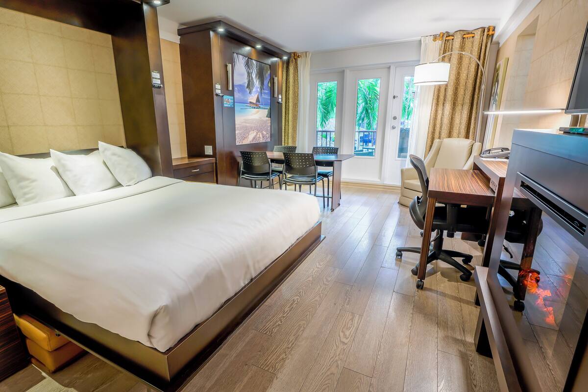 A hotel room with a large bed, a desk, a chair, and a view of the outdoors.