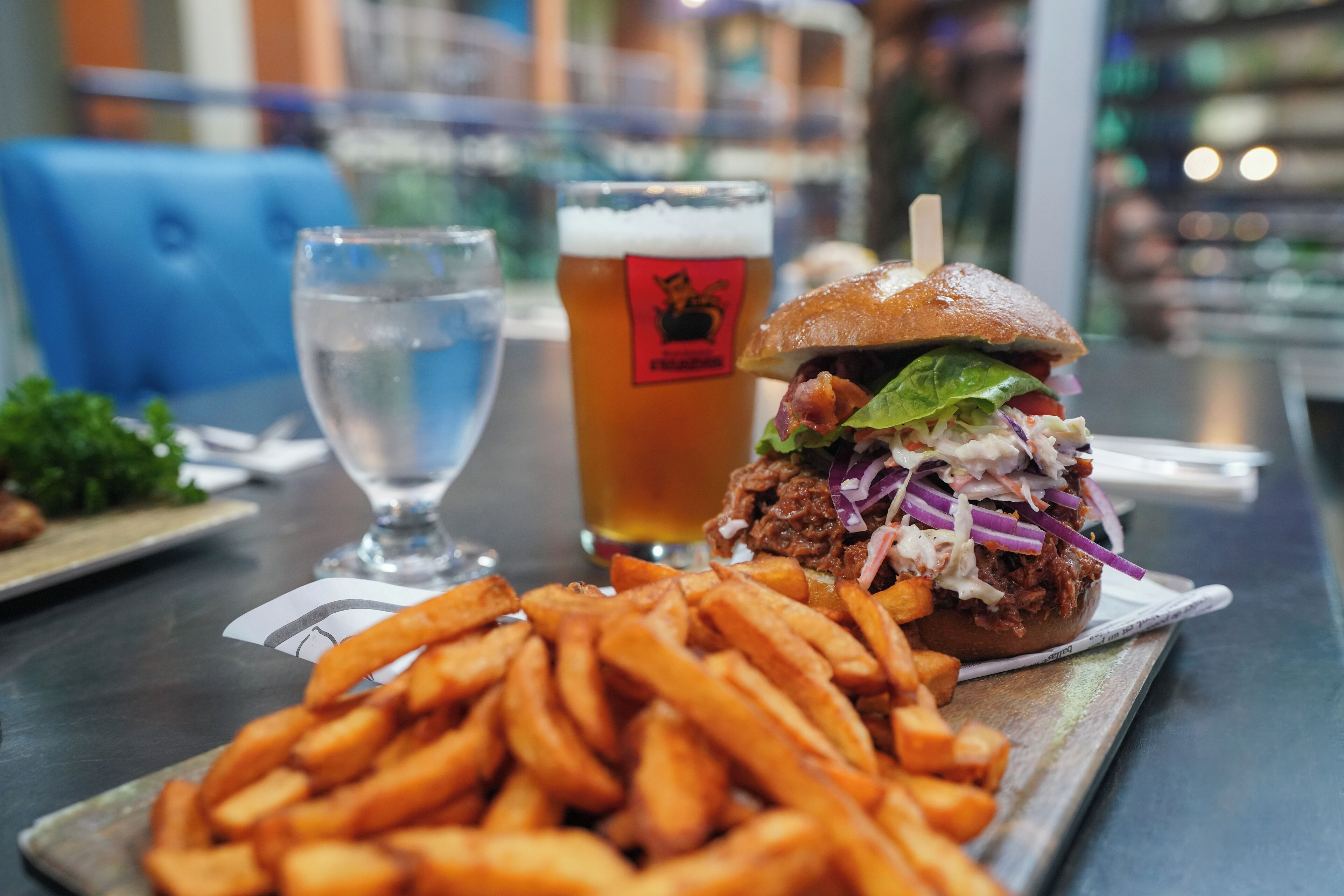 Eine Mahlzeit bestehend aus einem Burger, Pommes und einem Glas Bier auf einem Tisch.