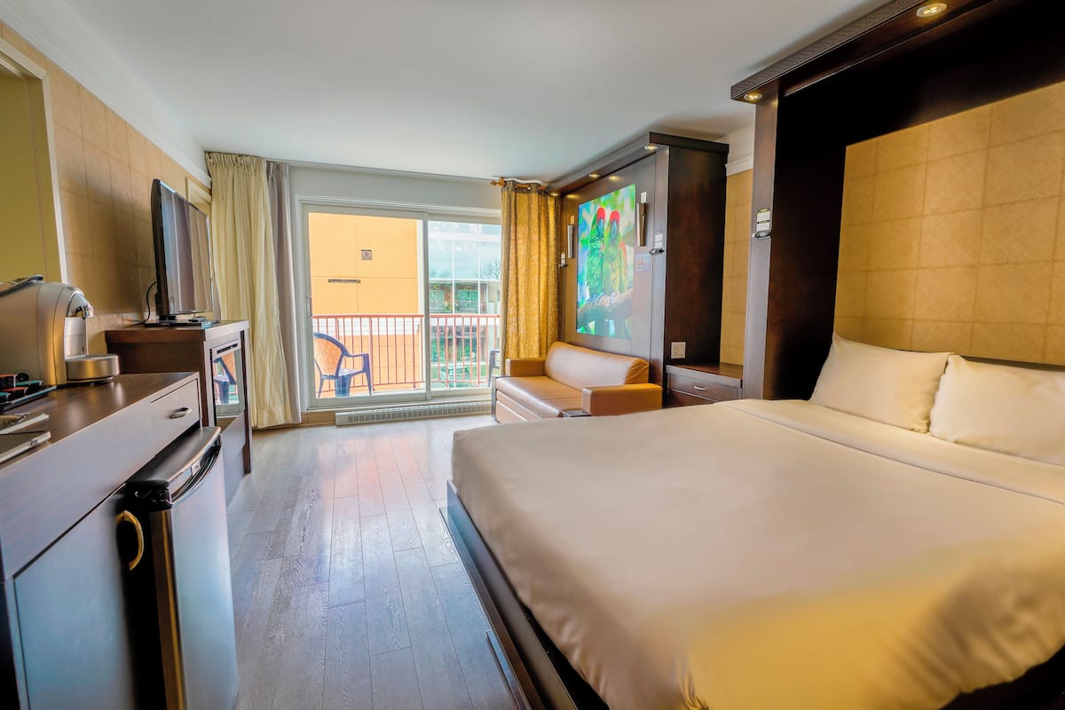A hotel room with a large bed, a desk with a computer, a chair, and a balcony with a view.