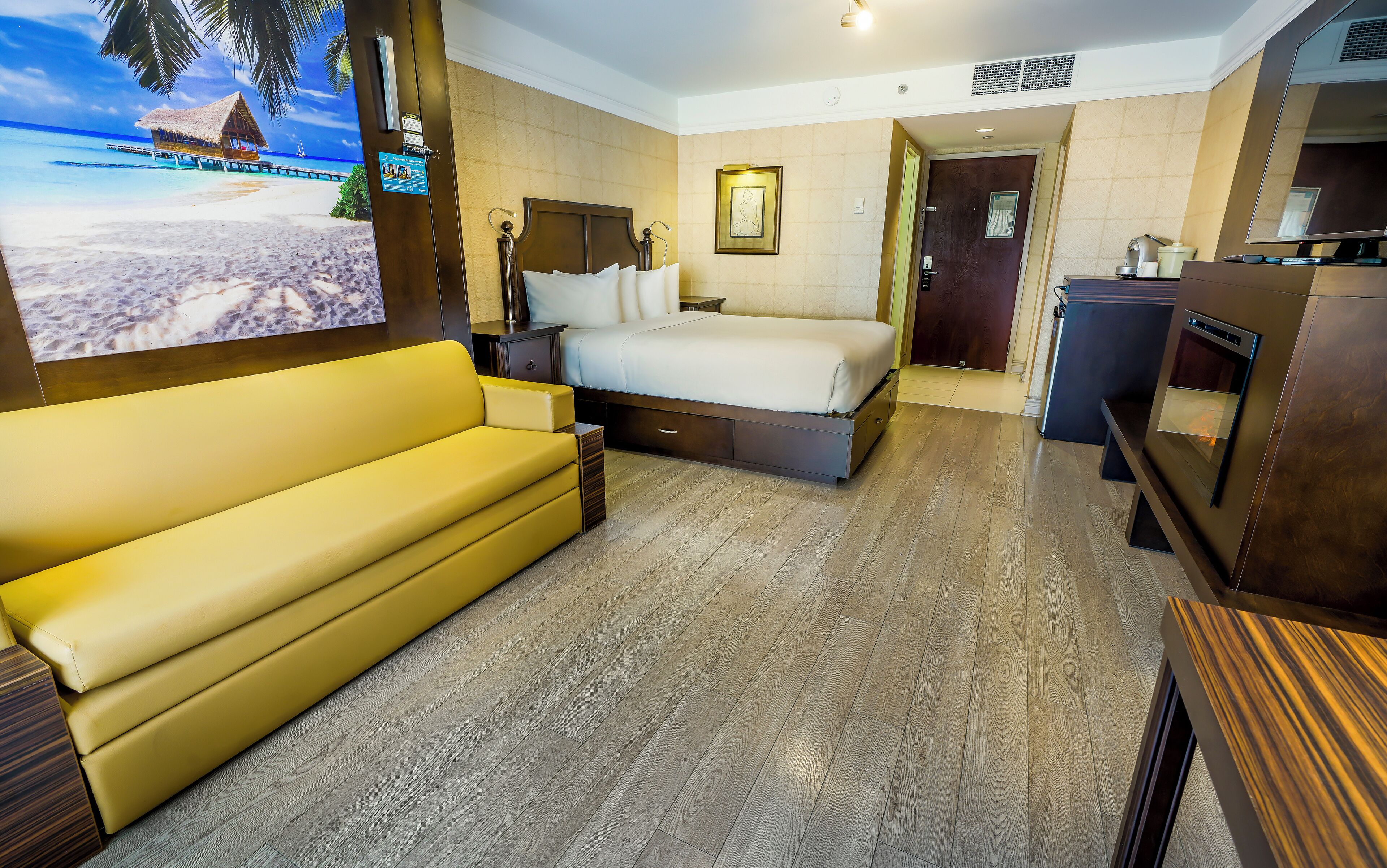 Una camera d'albergo con un letto, un divano giallo, una televisione e un pavimento in legno.