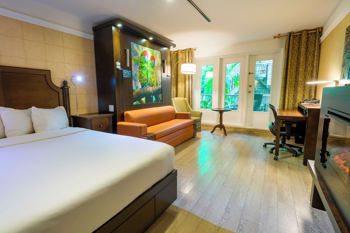 A hotel room with a large bed, a sofa, a desk with a computer, and a window with a view of greenery.