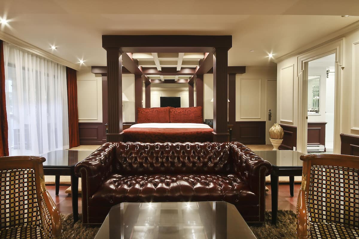 A hotel room with a large bed, a leather sofa, and a dining table.