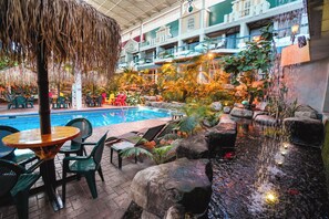 Uma área interna com piscina, cadeiras de descanso, uma mesa e uma cascata.