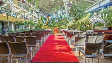 An indoor venue with a red carpet aisle, wicker chairs, and potted plants.
