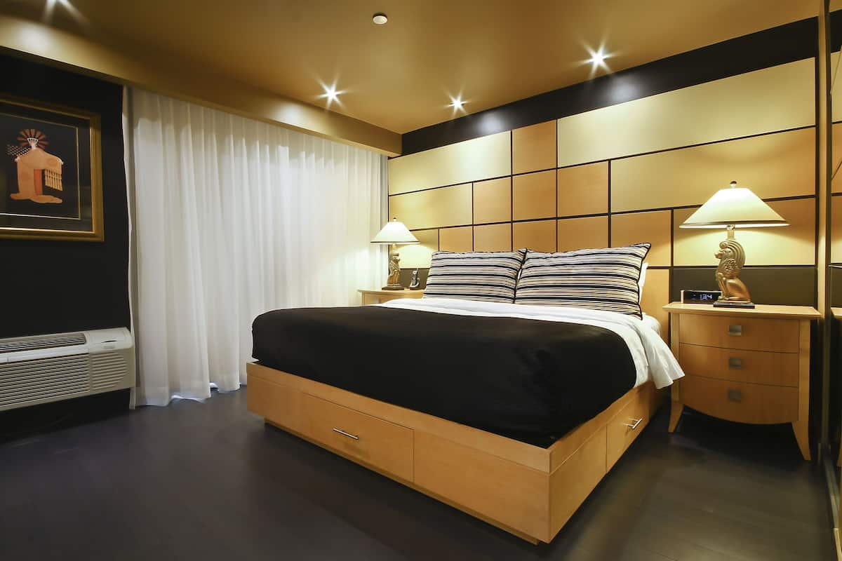 A modern hotel room with a large bed, two bedside tables with lamps, a wall-mounted air conditioner, and a framed picture on the wall.