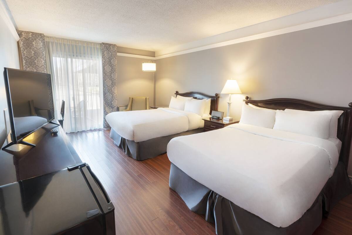 A hotel room with two beds, a desk, a TV, and a window with curtains.