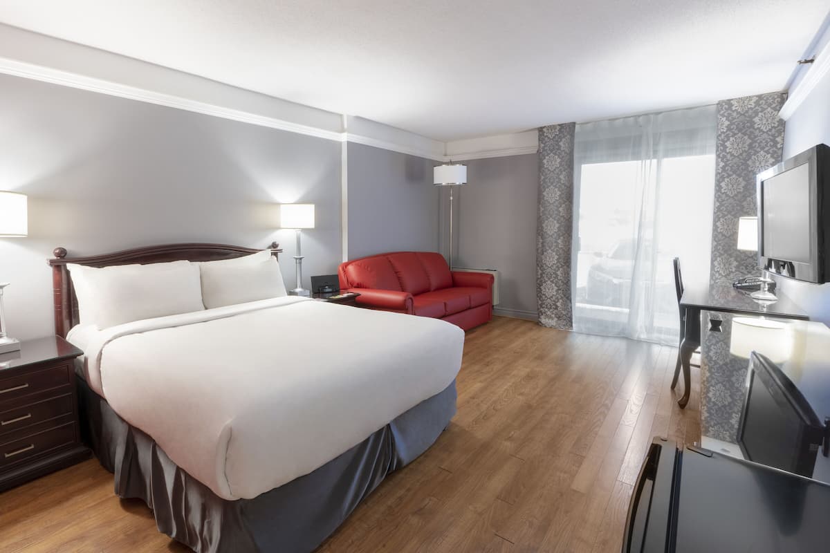 A hotel room with a large bed, a red sofa, a desk with a TV, and a window with curtains.
