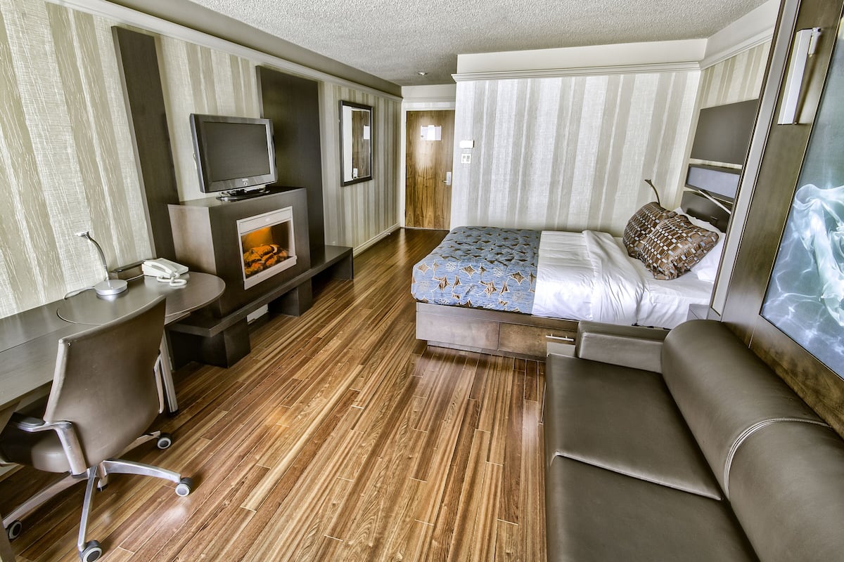 A hotel room with a bed, a desk with a chair, a television, and a fireplace.