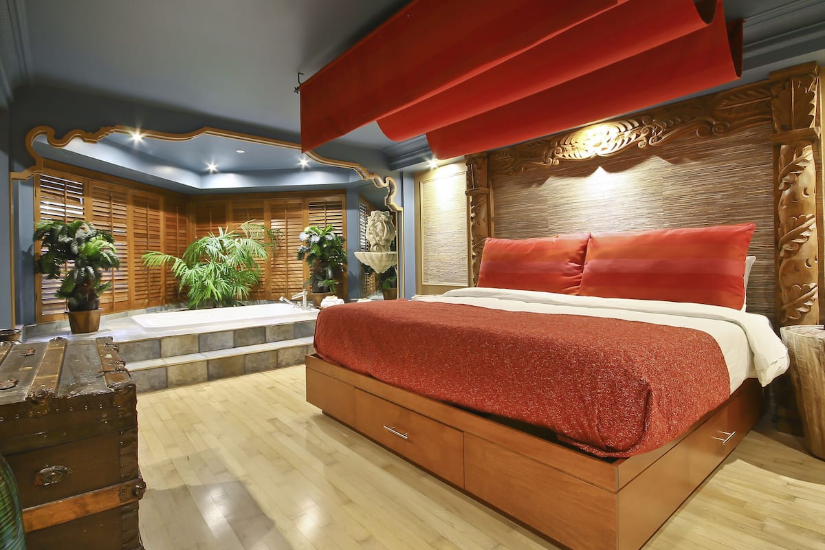 A spacious bedroom with a large bed, wooden headboard, and a red accent wall.