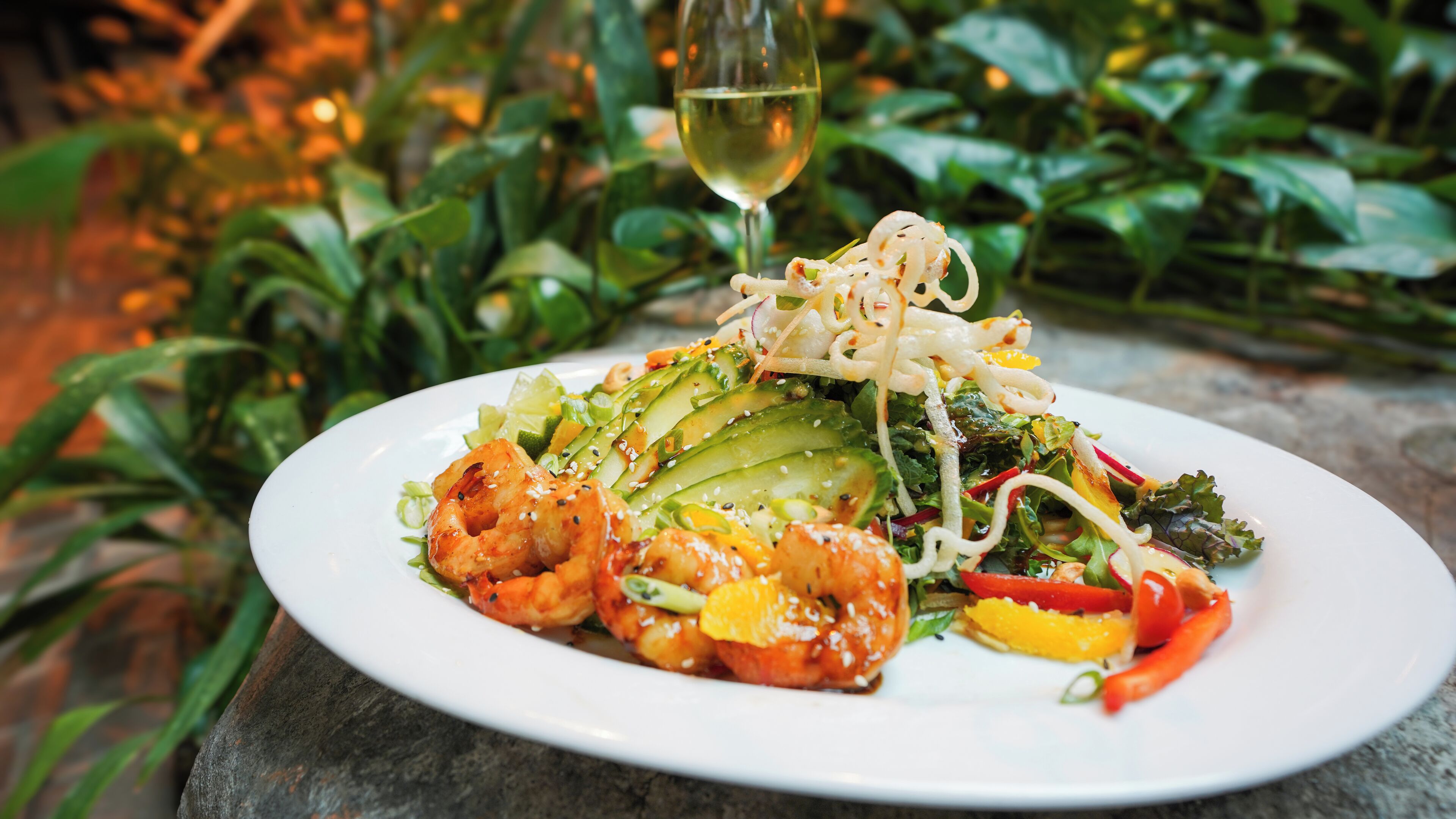 A plate of food with shrimp, avocado, and vegetables, accompanied by a glass of white wine.