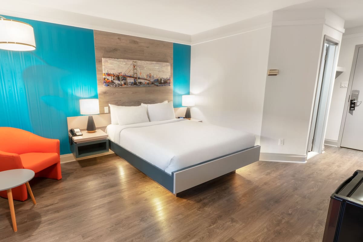 A modern hotel room with a large bed, a nightstand, a desk, and a chair.