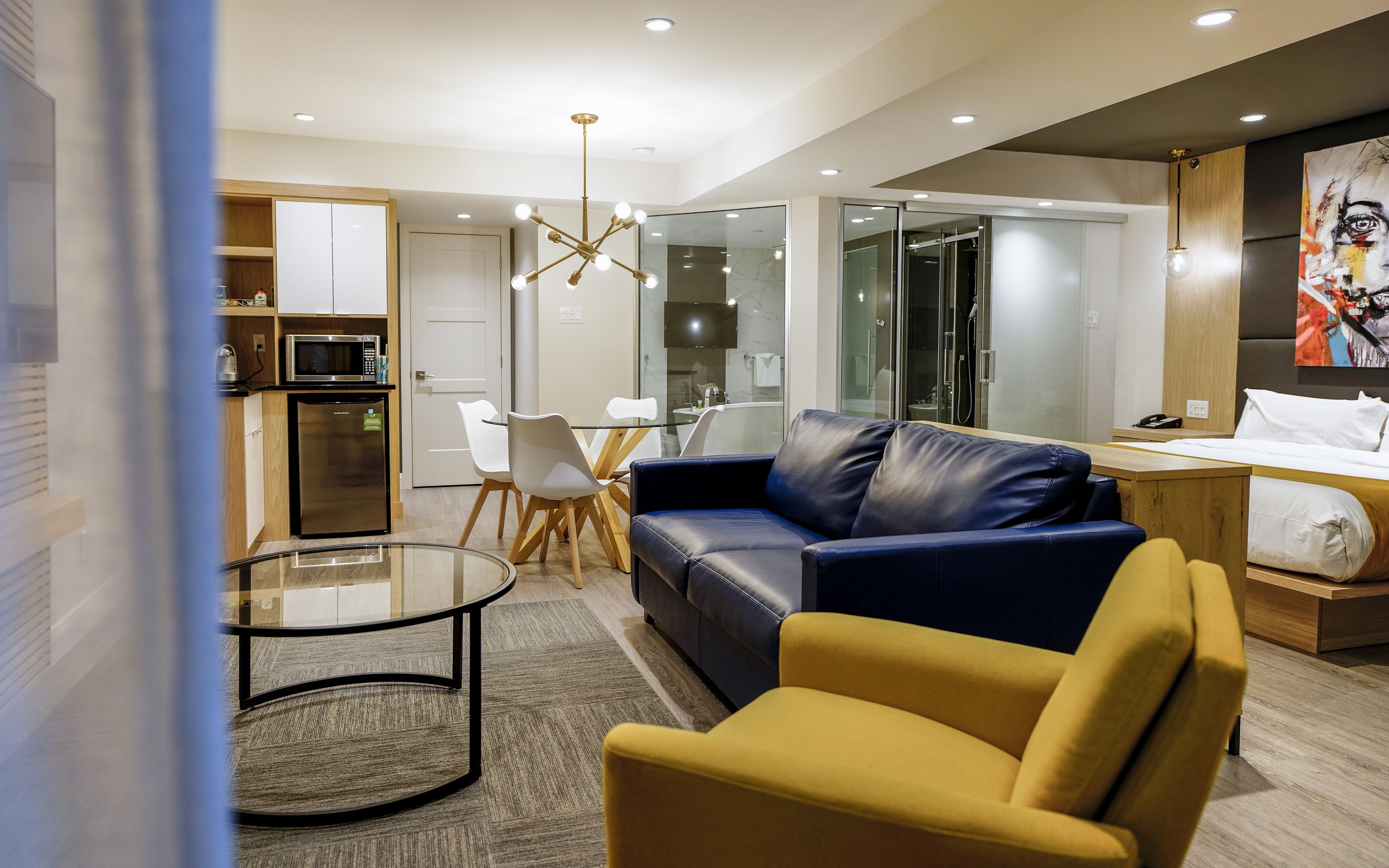 A modern living room with a leather sofa, a yellow armchair, a glass coffee table, and a dining area with a white table and chairs.