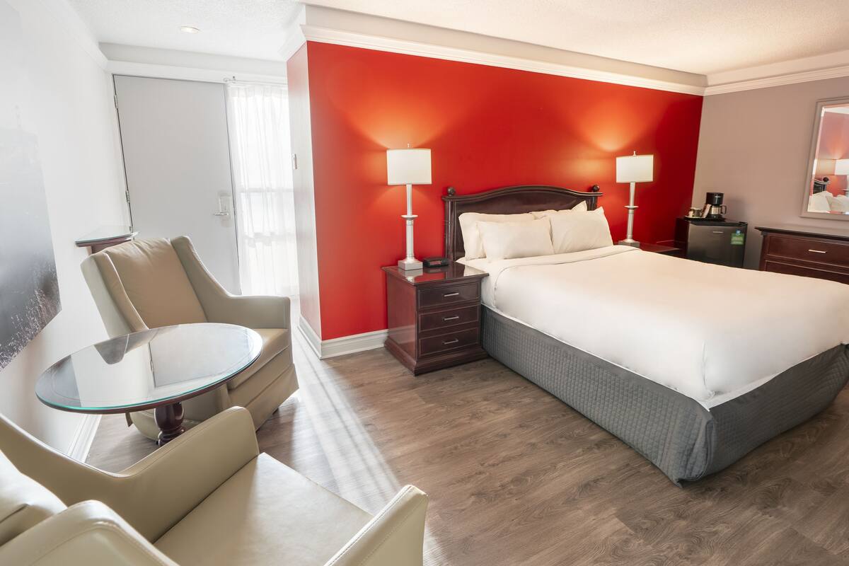 A hotel room with a bed, bedside tables, a chair, a small table, and a mirror.