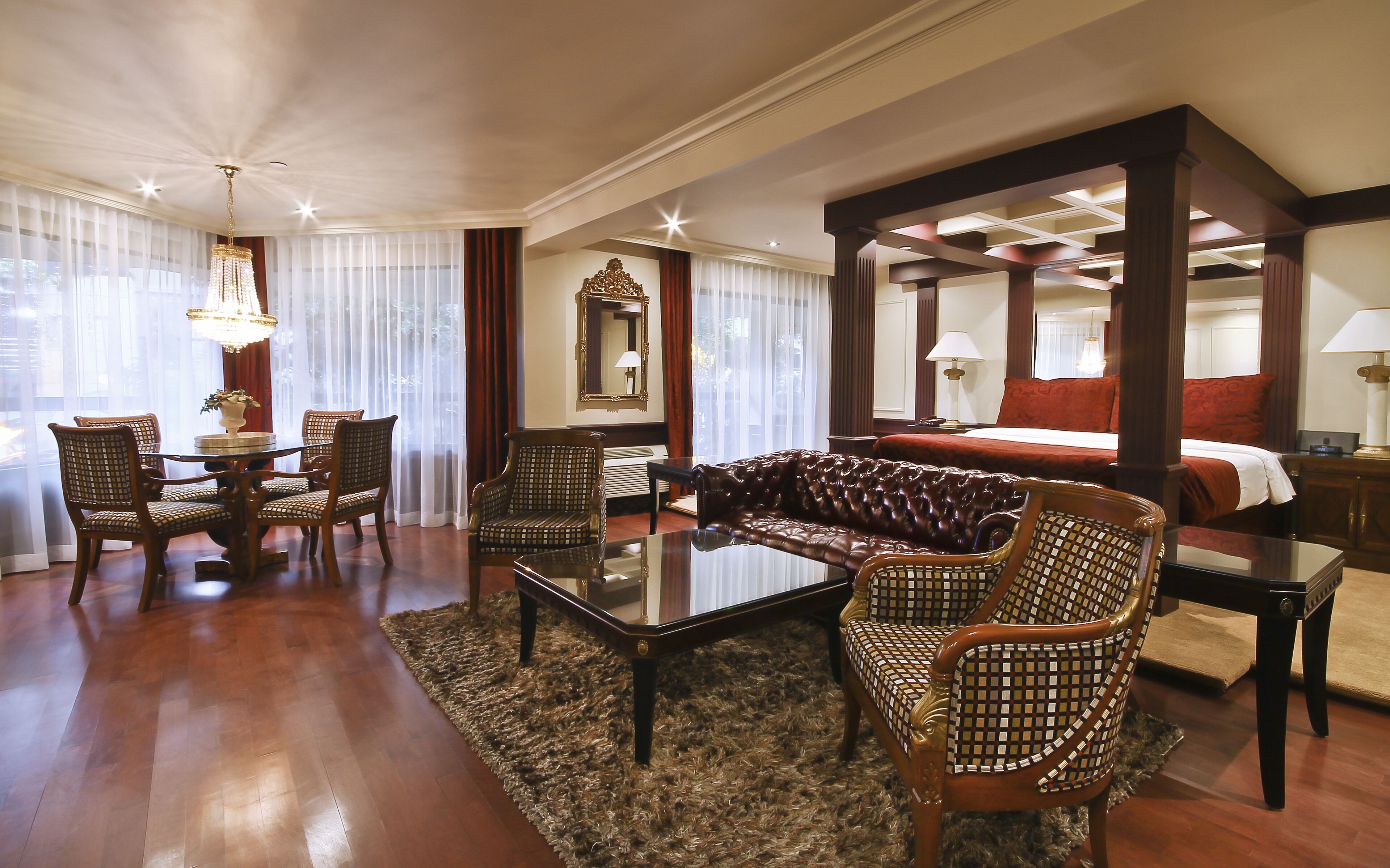 Une chambre d’hôtel dotée d’un grand lit, d’un coin salon avec un canapé et des fauteuils, d’une table à manger et d’un lustre.