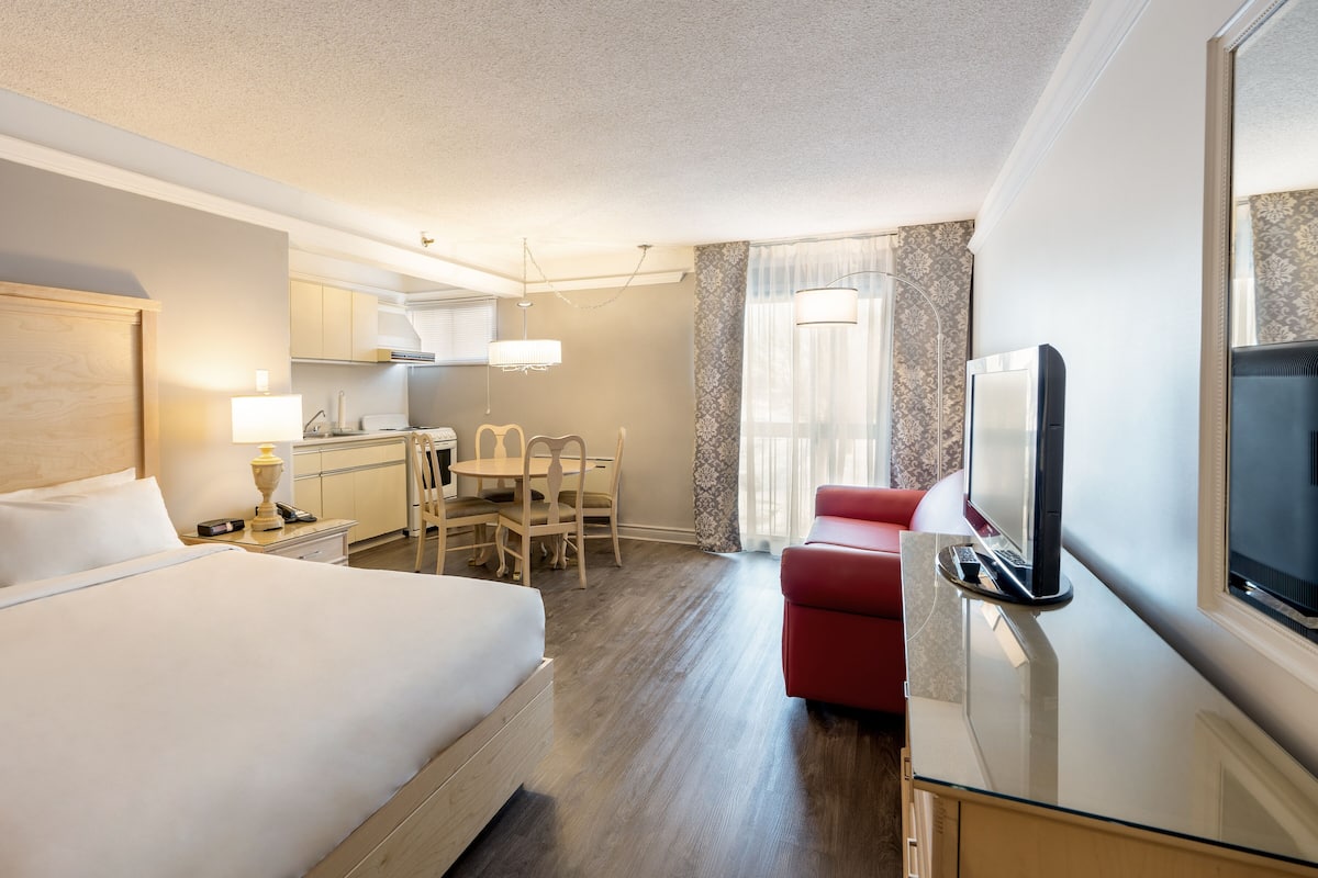 A hotel room with a bed, a desk with a chair, a TV, and a window with curtains.