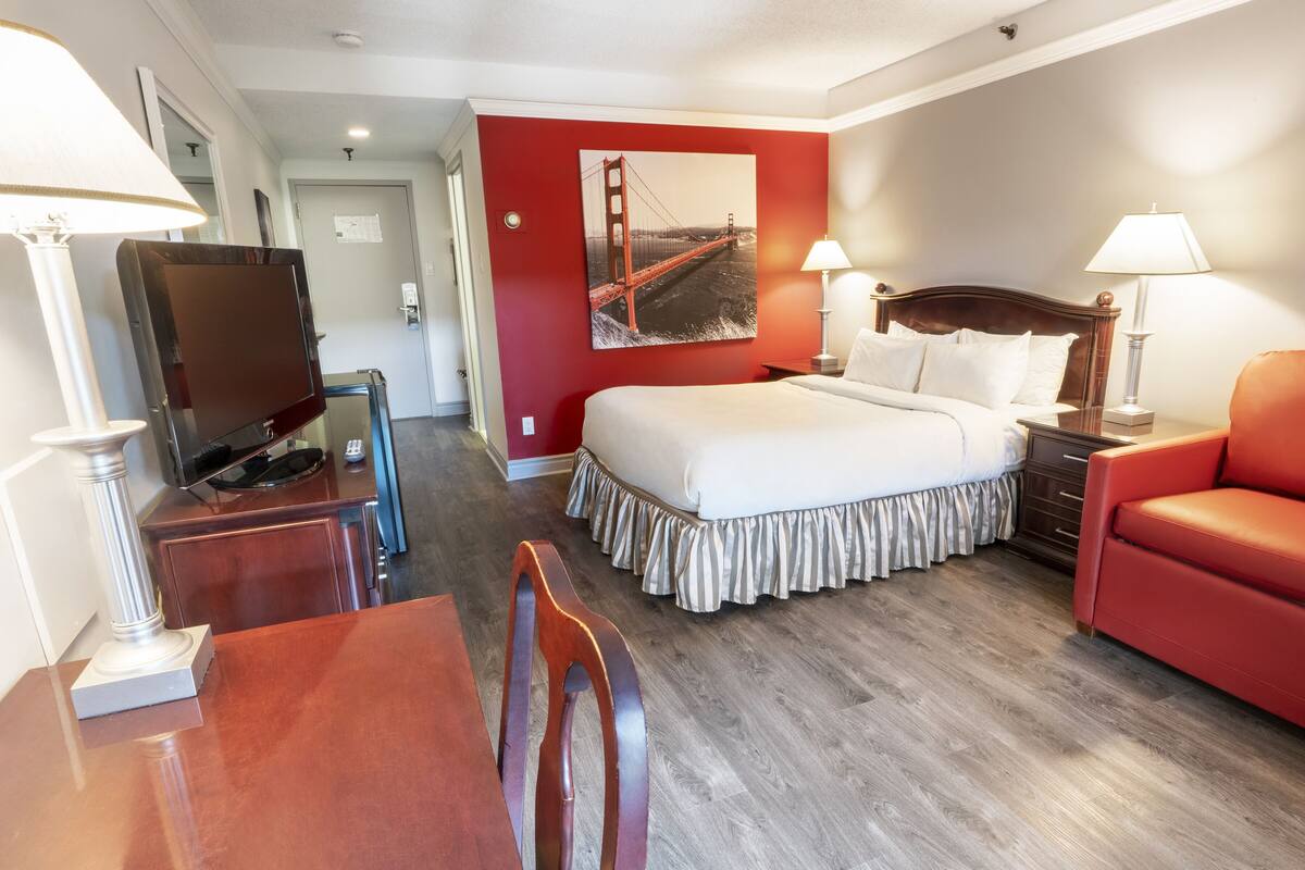 A hotel room with a bed, a TV, a desk, a chair, and a red couch.