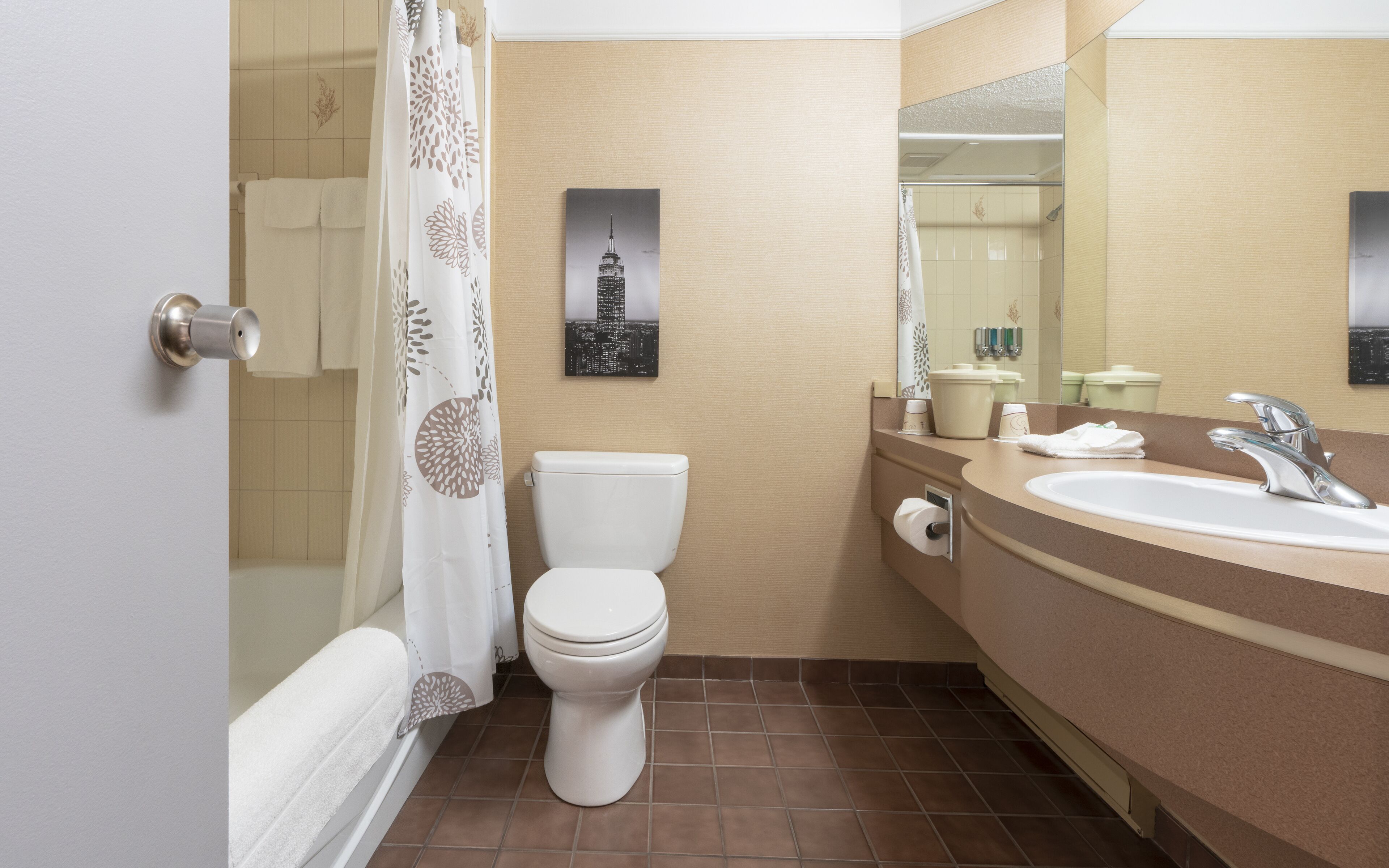 A bathroom with a toilet, shower, sink, and a mirror.