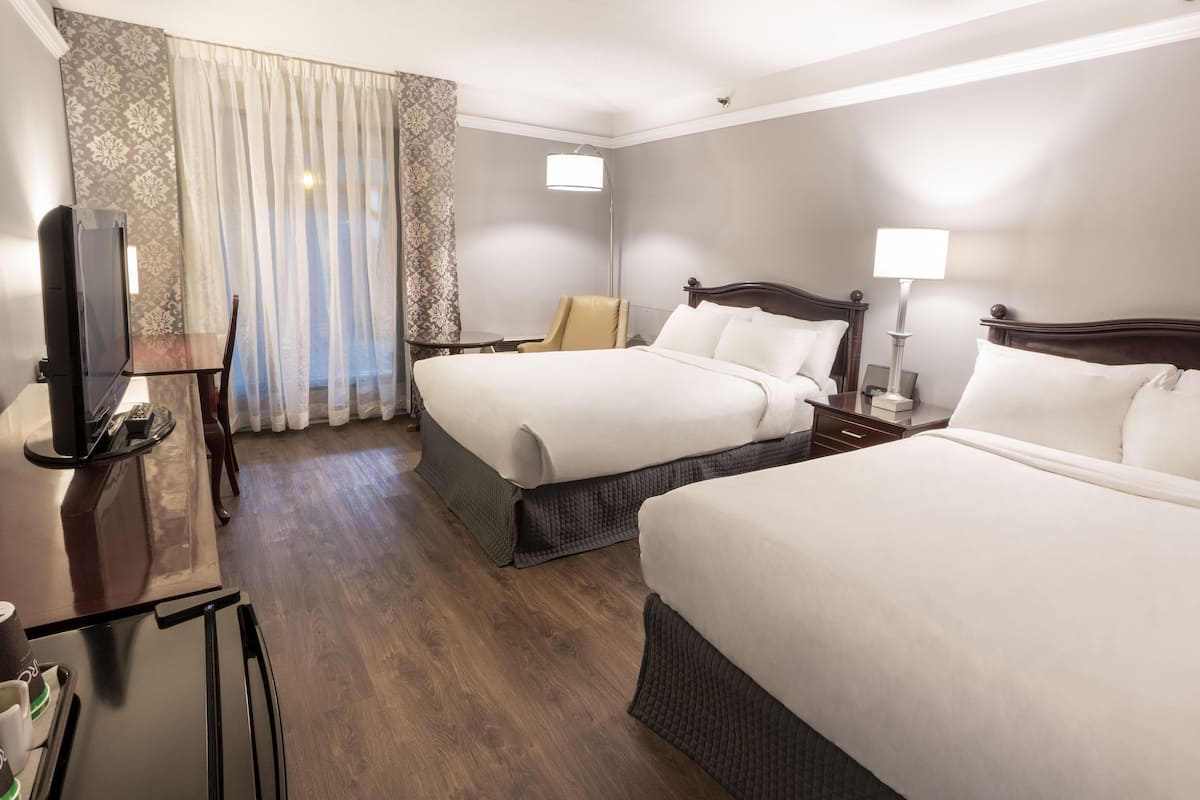 A hotel room with two beds, a TV, a desk, and a chair.