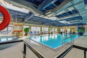 Una piscina interior con agua azul cristalina, rodeada de sillas de descanso y plantas en macetas.