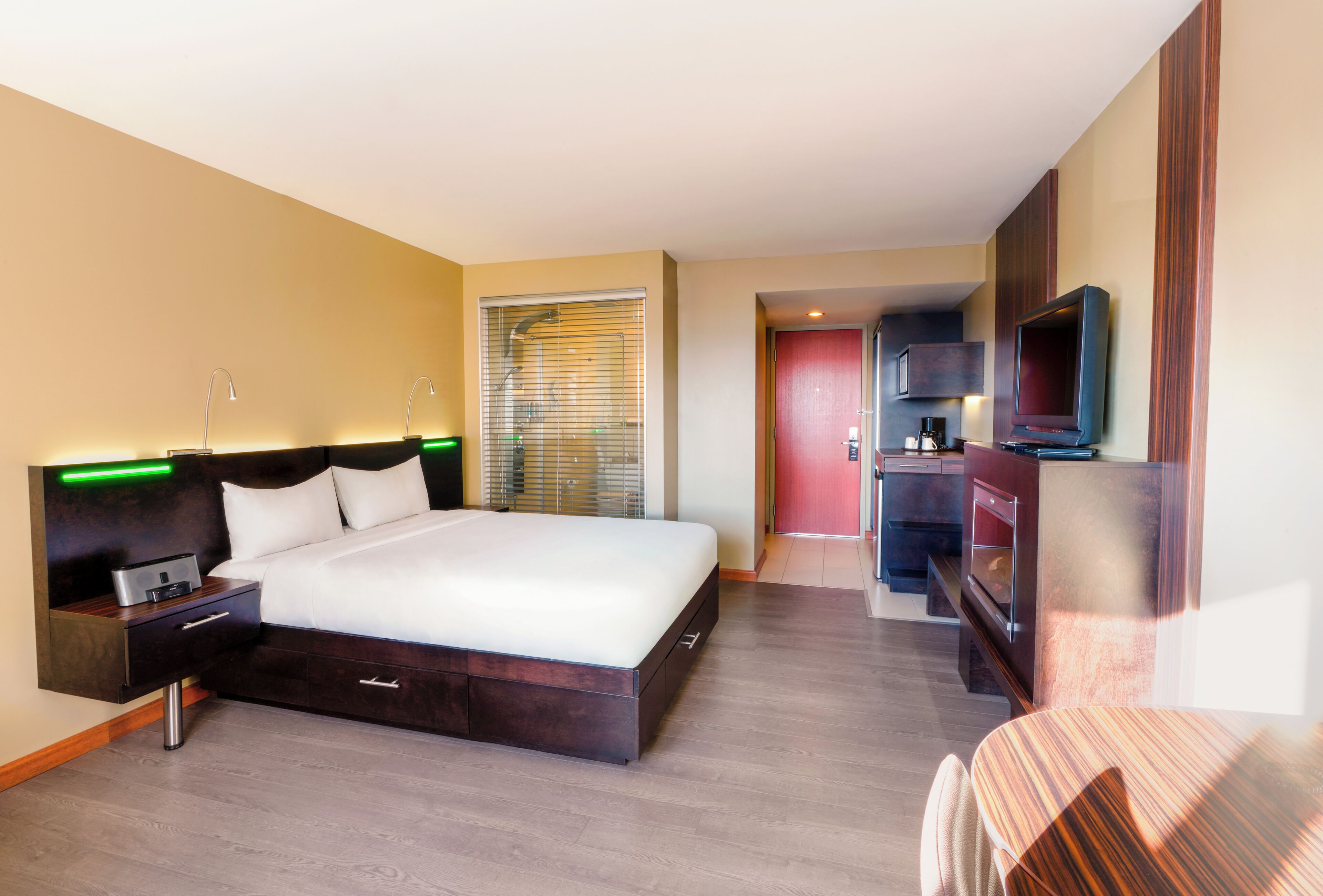 Une chambre d’hôtel moderne dotée d’un grand lit, de tables de chevet, d’une télévision et d’une kitchenette.
