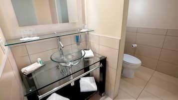 Um banheiro moderno com uma pia de vidro, vaso sanitário e espelho.