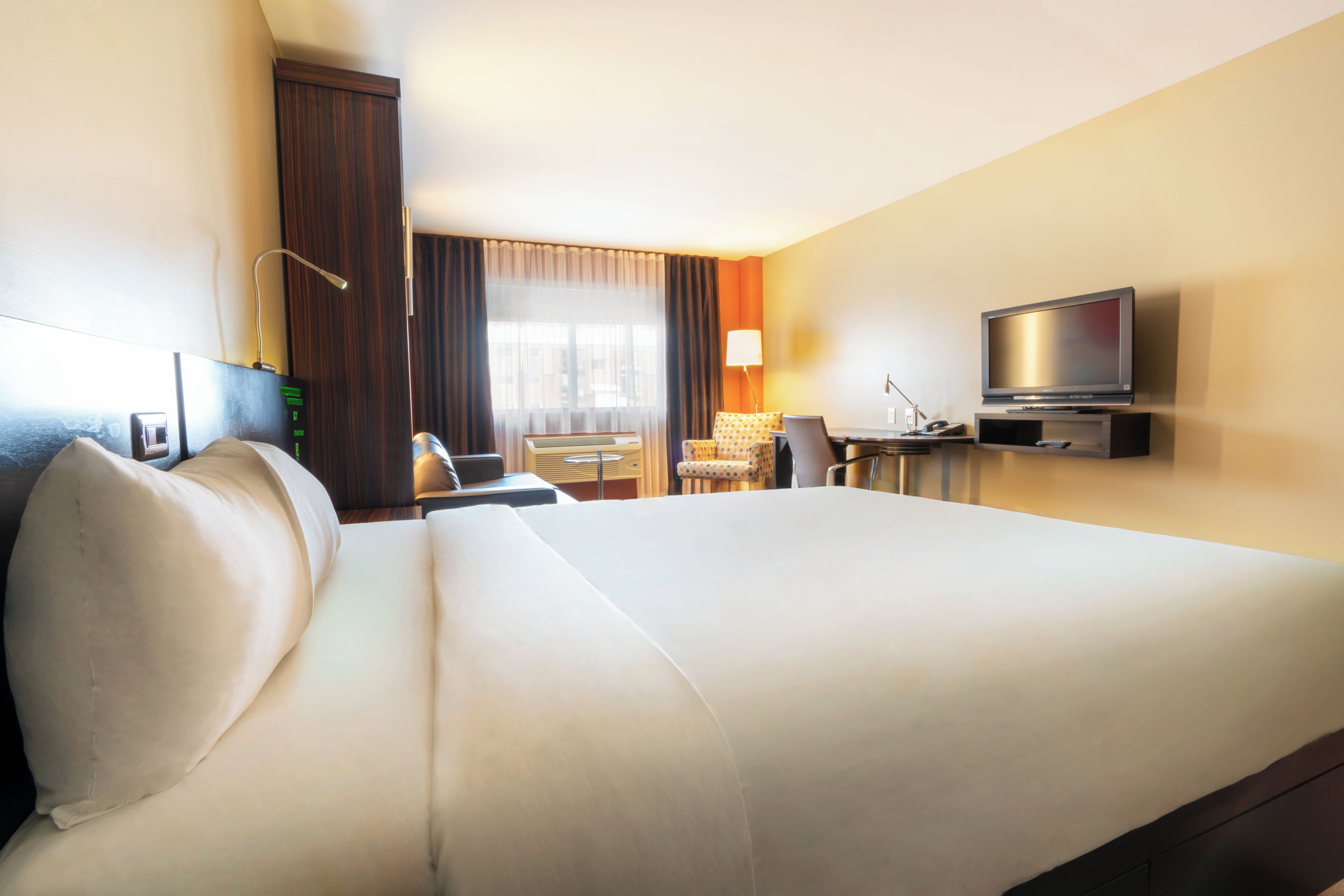 A hotel room with a large bed, a desk with a chair, a television, and a window with curtains.